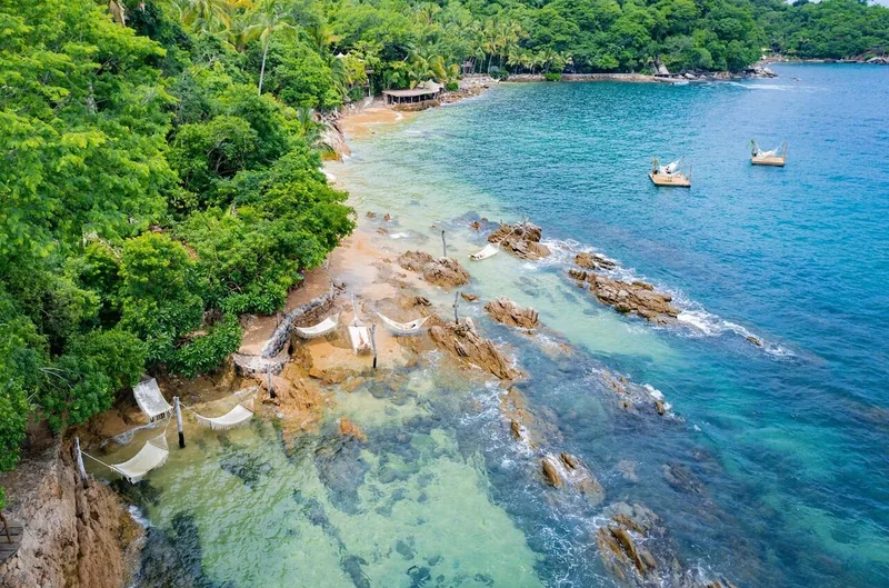 Vue aérienne d'un rivage rocheux de jungle, avec des hamacs au-dessus des rochers et une eau limpide