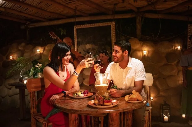 Ein Paar stößt über Tellern mit Essen an einem Holztisch bei Kerzenlicht an