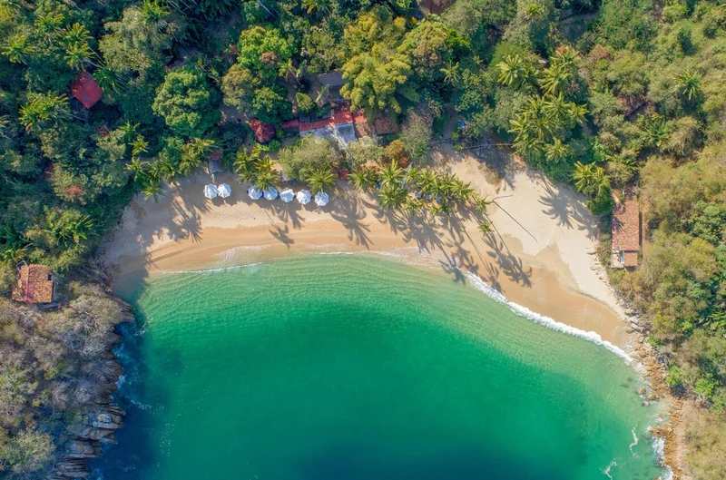 Luftaufnahme einer kleinen hufeisenförmigen Bucht mit Sandstrand, Sonnenschirmen und türkisfarbenem Wasser